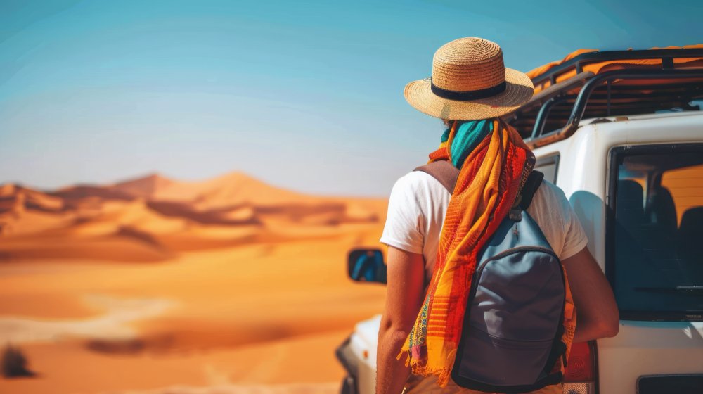 Traveller looking out over desert dunes beside a 4x4